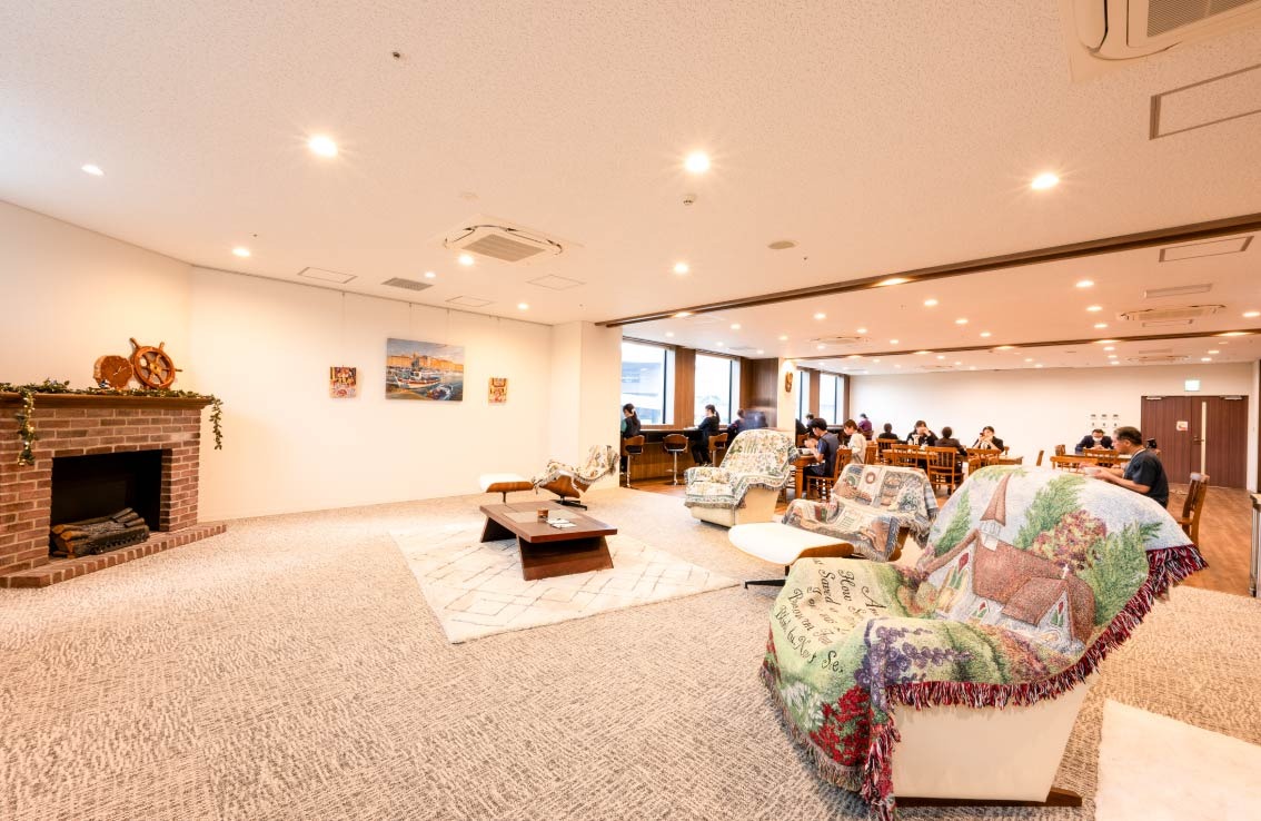 広々とした日当たりのいい休憩スペースで、スタッフの皆さんがくつろいでいる様子。ソファや暖炉もあり、開放的な雰囲気。