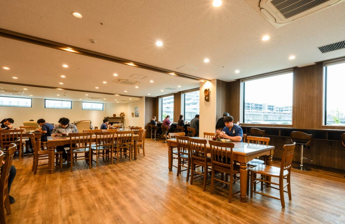 職員専用の食堂で病院スタッフの皆さんが食事をしている様子。大きな窓と、ゆとりのあるスペースで、明るい雰囲気の食堂です。