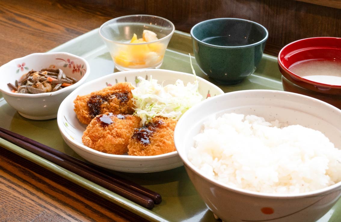 ランチセット（白いご飯、ソースのかかった揚げ物とキャベツ、小鉢のおかず、味噌汁、デザート、お茶）